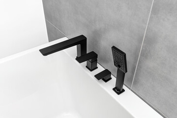 A modern, free standing wall mounted bathtub with a black matt tap, standing in a bathroom lined with ceramic tiles.