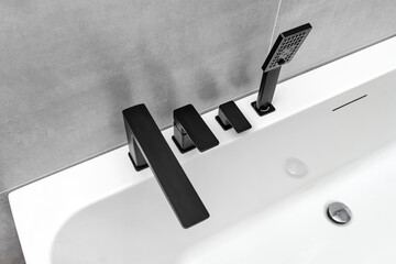 A modern, free standing wall mounted bathtub with a black matt tap, standing in a bathroom lined...
