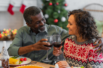 joyful african american father and daughter clinking glasses of red wine during christmas dinner