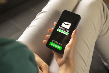 Subscribe newsletter concept on mobile phone or smartphone. Woman indoors holding mobile phone with newsletter join, sign up and register page