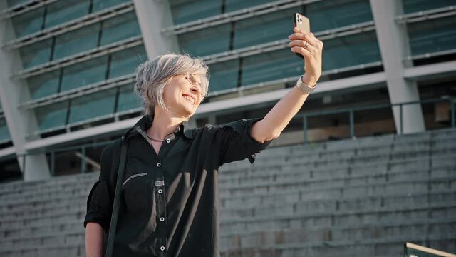 Happy adult woman, feminine health and menopause concept. Mature lady is taking a selfie against the background of a modern business center