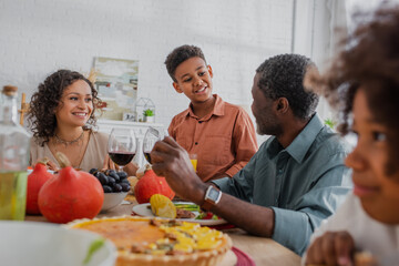 smiling african american boy talking to grandfather during thanksgiving dinner with family