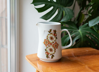 Mid-century modern porcelain jug on a wooden table with plants in the background