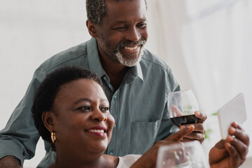 African american woman pointing at smartphone near husband with wine at home