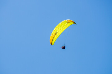 A yellow paraglider flies in the blue sky