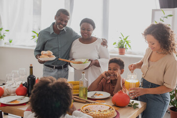 Smiling african american grandparents holding food near family and thanksgiving dinner