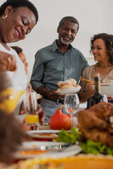 African american grandfather holding food near family and thanksgiving dinner