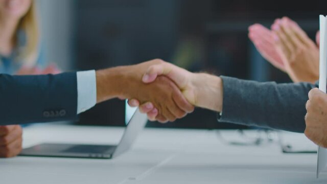 Cropped view of man holding just signed business agreement and shaking hand of business partner. Modern open space office interior.