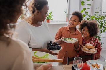 Smiling african american kids holding food near granny and mother during thanksgiving dinner