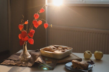 Cozy home breakfast with apple pie, bouquet of red flowers on a table in a sunny room