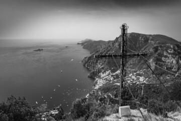 black and white photo of cross of Vagnulo on a path of the Amalfi coast with Li Galli islet,  Positano and Capri in the background. Agerola, Positano, Campania, Italy