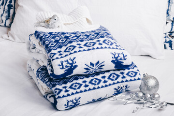 Knitted sweaters with deer pattern stacked in a pile on the bed