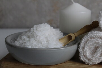 salt for bath scrub home body care. Coarse salt lies in a gray bowl plate with a wooden spoon towel candle on a gray background. Spa relaxation