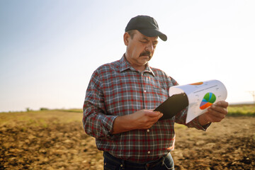 Farmer watching some charts and checks quality of soil. Agriculture, gardening, business or ecology concept.