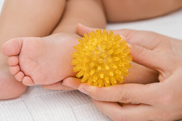 Mom massages a newborn baby with a yellow rubber ball with spikes