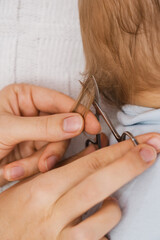 A hand holding a small pair of scissors cuts a lock of hair from the head of a sleeping baby
