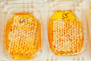 Texture of honeycombs close up. Yellow wax honeycombs with honey in plastic containers. Sale of homemade honey at the fair.