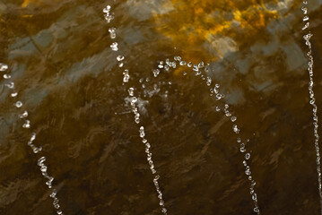 Water drops from a fountain close up. Jet fountain on a sunny day. Sharpness on the front drops of...