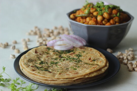 Perfectly round Paratha. Indian flatbread made of wheat flour topped with sesame seeds and coriander leaves served with white chickpea gravy commonly known as chole masala
