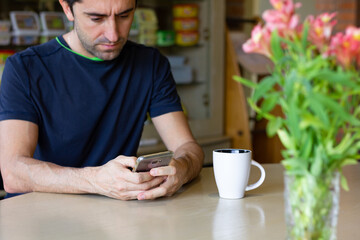 Man with cellphone on table and coffee cup and flower vase on sides. Stressful lifestyle, busy business work, nervous concepts