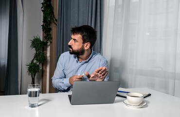 Young businessman sitting in an office and shields or hide a laptop screen with his hand because a...