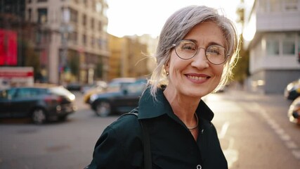 Close up portrait of a mature stylish business woman in the middle of a busy city street in the center. Portrait of an active aged woman near the business center. Slow motion