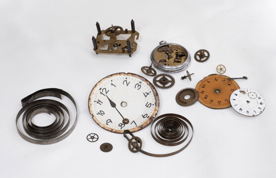 disassembled parts of an antique clock, clock hands, gear wheels, torsion springs, clock faces, scrapped antique clock parts, sprocket , dials, piano springs and broken mechanism on a white background