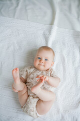 A cute little girl 5 months old lies on her stomach on the bed at home.