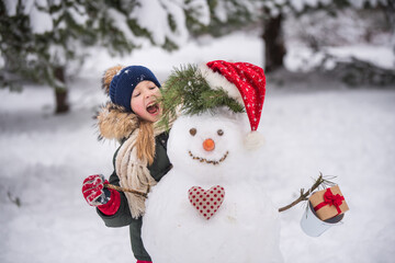Happy blonde cute child girl plaing with a snowman