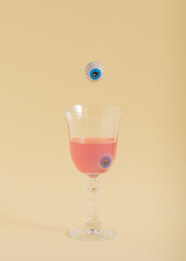 Spooky Halloween concept with an eye falling into a drinking glass. Vertical aesthetic composition, creative season concept. Pastel beige background.