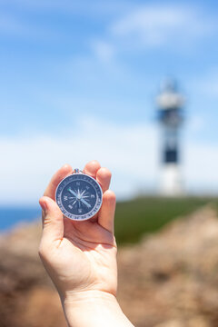 Hand holding a compass in front of a lighthouse by the sea, during a sunny day, vertical shot, concepts, selective focus.
