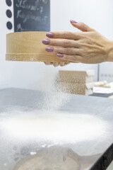 Neat female hands with manicure sift flour through a sieve. Preparation of dough for baking