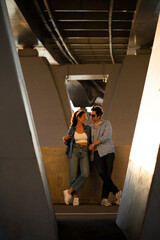 Fototapeta na wymiar Loving young couple embracing at sunset standing over urban background under bridge. Trendy man and woman in hipster sunglasses and street style stylish clothes hugging enjoy spending time together