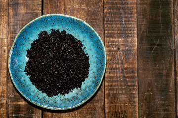 Healthy food black rice in blue plate on wood background.