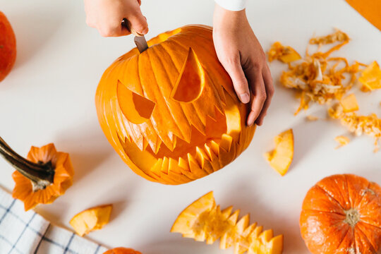 Happy halloween, decoration and holidays concept. Young woman hands with knife carving pumpkin or jack-o-lantern on white table background at home. Close-up, top view, flat lay