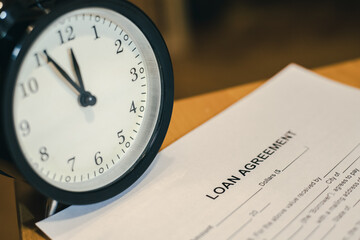 Unpaid loan - loan agreement - blank paper draft of document on a wooden table and classic clock...