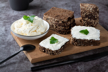 Rye bread on a wooden cutting board with curd cheese and ricotta and herbs. Decorated with green herbs