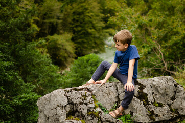 Naklejka na ściany i meble A boy sits on a large stone in nature