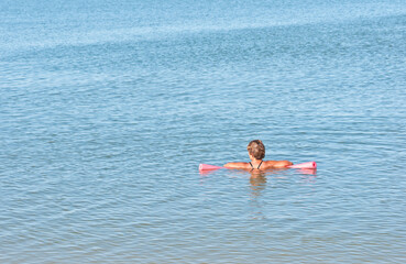 back view, far distance, of a middle aged female resting on a pink float in calm waters of gulf of Mexico, on a sunny afternoon
