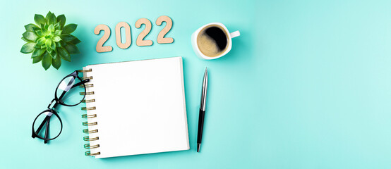 New year 2022 goals on desk. 2022 resolutions with open notebook, coffee cup, eyeglasses, plant...