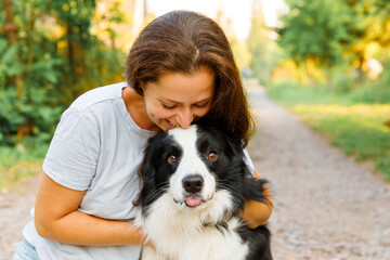 Smiling young attractive woman playing with cute puppy dog border collie on summer outdoor background. Girl holding embracing hugging dog friend. Pet care and animals concept.