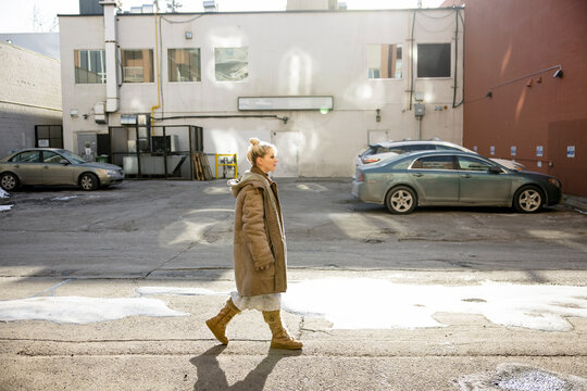 Young woman in boots and winter coat walking in sunny city alley
