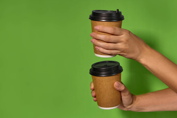 Close-up on a green background, women's hands hold two paper cups with coffee in a stand. Coffee or tea with you. Promotion two for the price of one, coffee delivery.