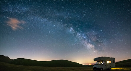 Panoramic night sky over Campo Imperatore highlands, Abruzzo, Italy. The Milky Way galaxy arc and stars over illuminated camper van. Camping freedom in unique hills landscape. © fabio lamanna