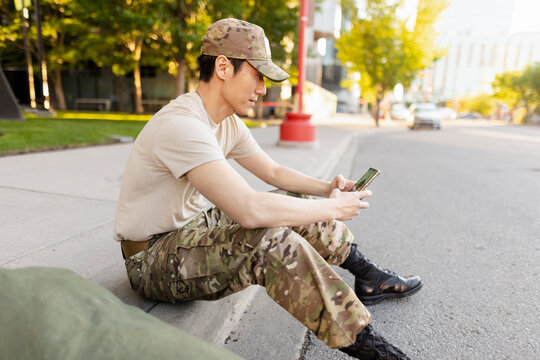 Soldier waiting on sidewalk, texting on phone