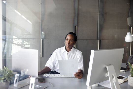 Corporate businesswoman with paperwork using laptop at desk