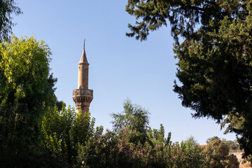 Obraz premium High minaret on a background of blue sky. View through the trees in a park. (Gaziantep, Turkey.)