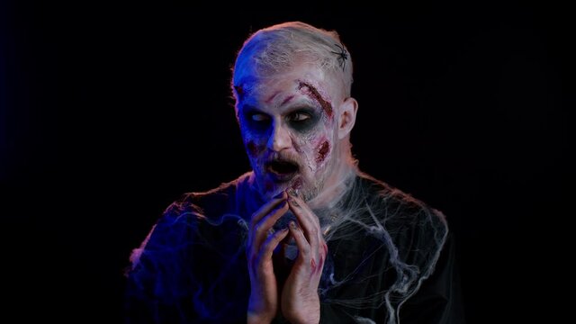 Frightening man with Halloween zombie bloody wounded face make-up, scared by police lights. Horror theme. Sinister undead guy isolated on studio black background. Voodoo rituals. Detention of criminal