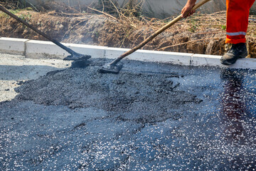 Road construction workers leveling hot asphalt pavement