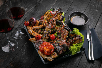 Assorted grilled meat with sauce and red wine on a black table.
